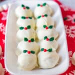 Snickerdoodle truffles coated in white chocolate, topped with a christmas sprinkle, and served on a white tray surrounded by holiday decor.