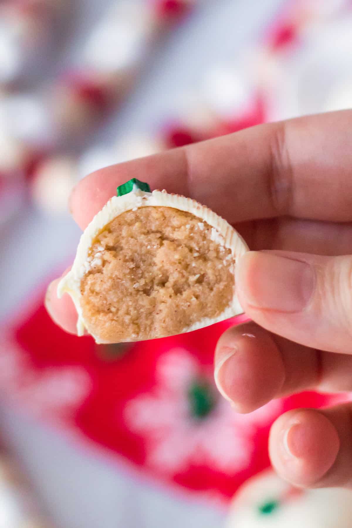 Hand holding snickerdoodle cookie dough truffle cut in half to show golden cookie mixture inside.