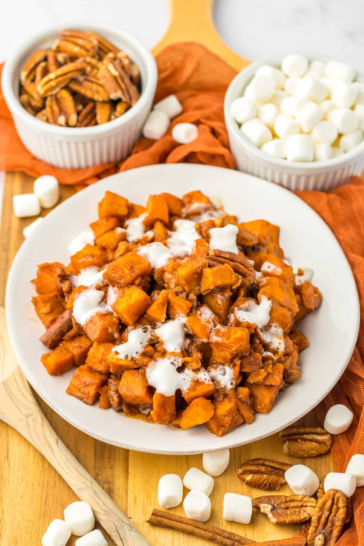 Slow cooker sweet potatoes served on a white plate with additional pecans and mini marshmallows surrounding it.