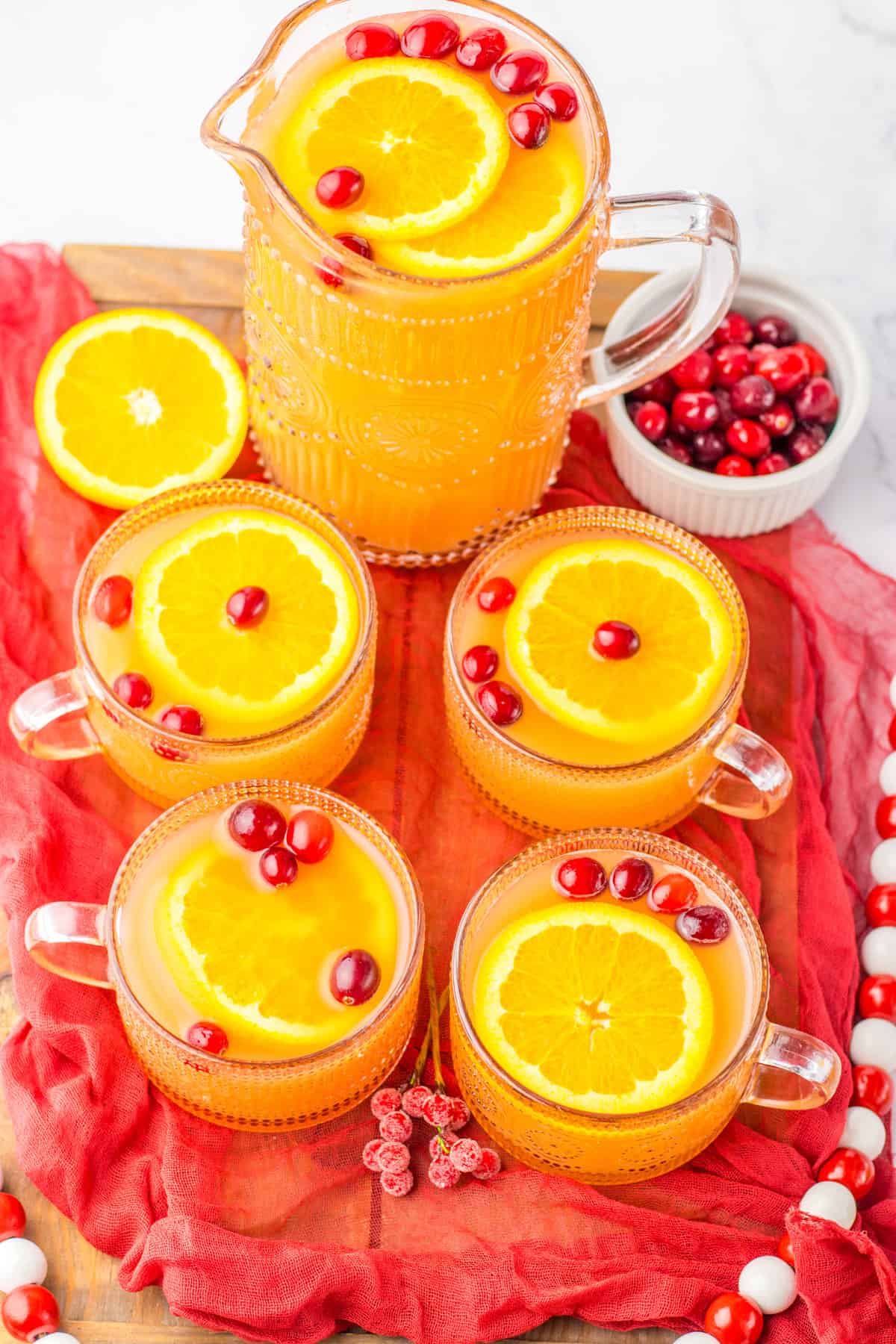 Non alcoholic Christmas punch with fresh orange slices and cranberries in a glass pitcher and in four glasses.