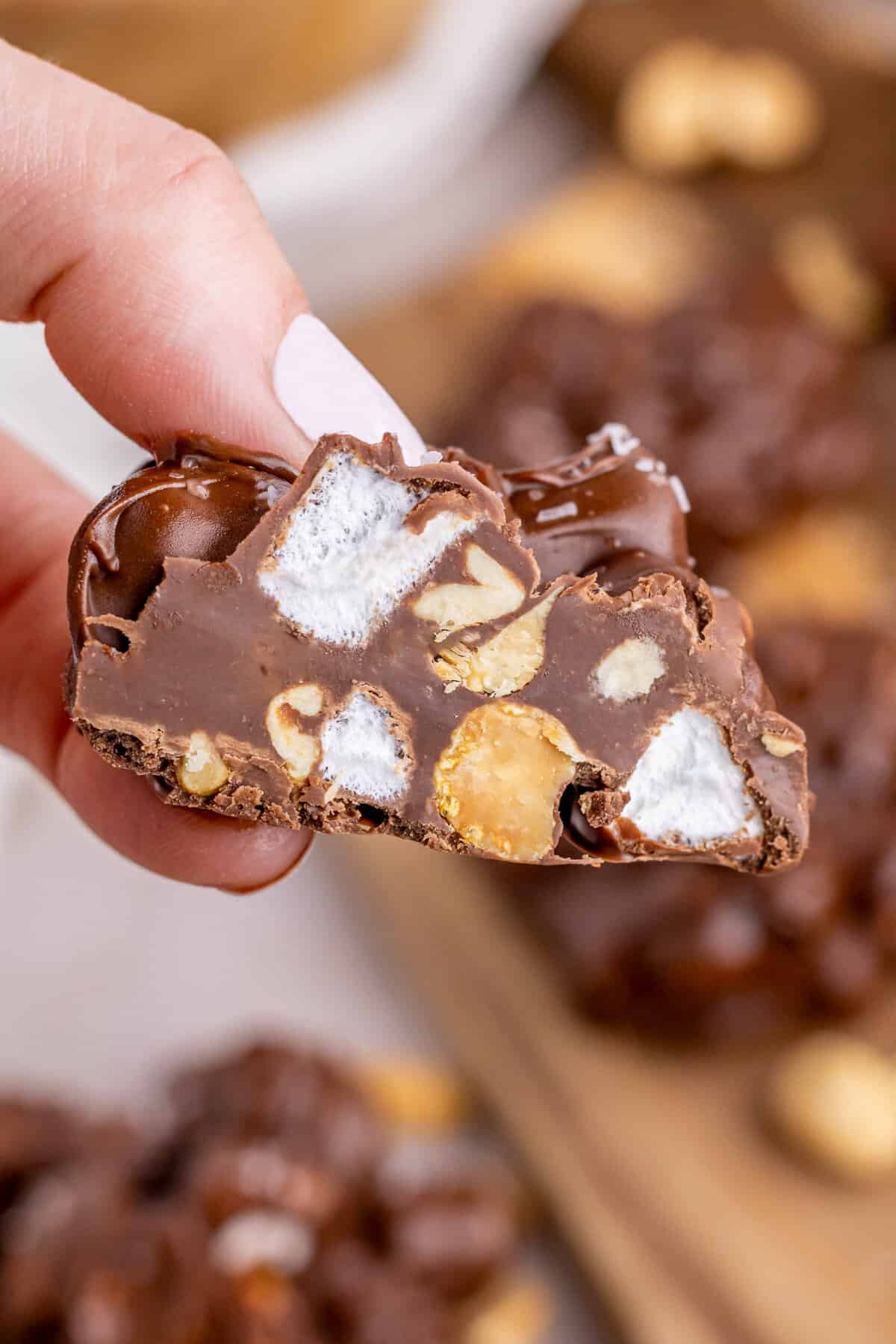 Hand holding piece of rocky road chocolate cut in half to show marshmallows and peanuts inside.