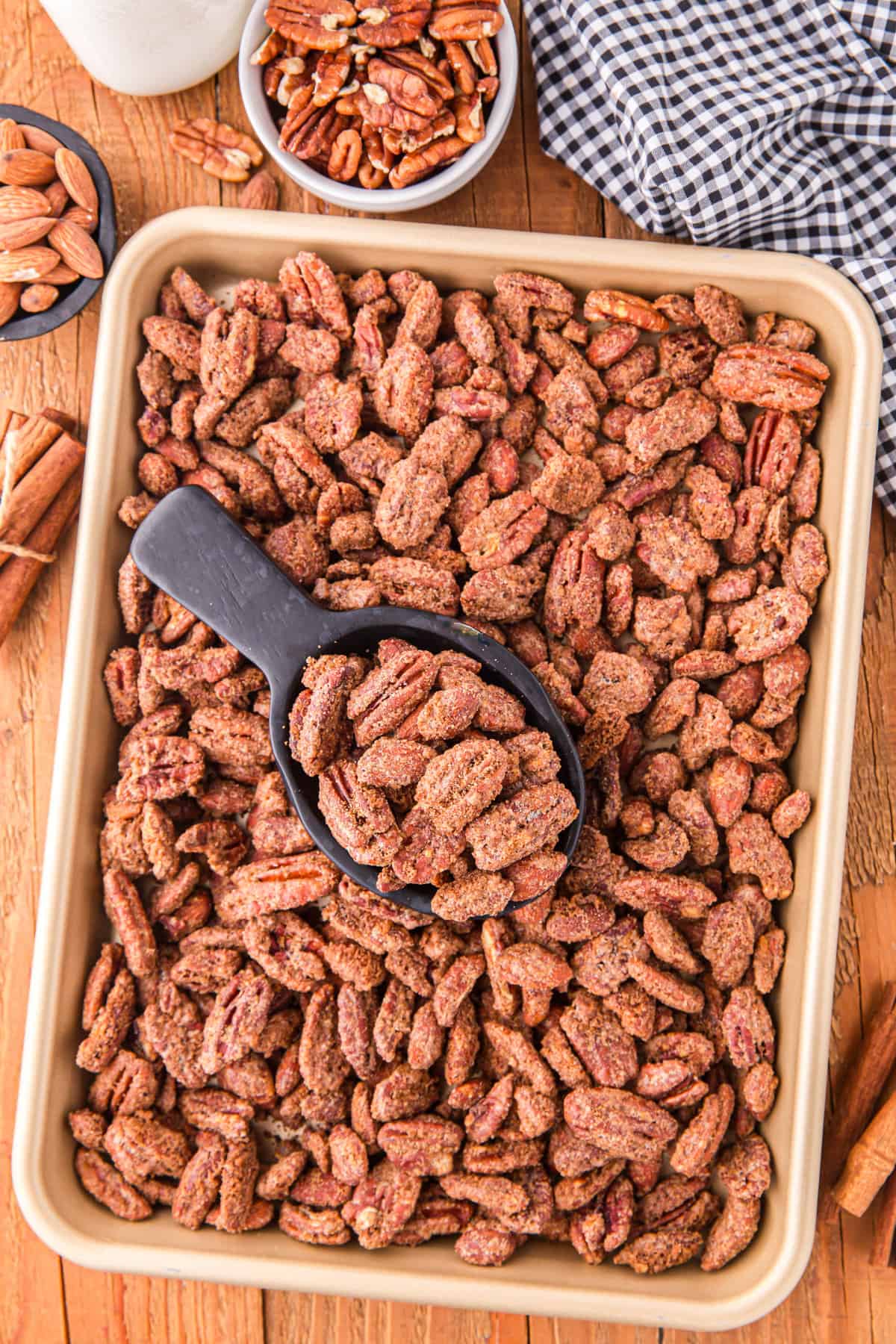 Candied almonds and pecans on a backing sheet with a small black scoop.