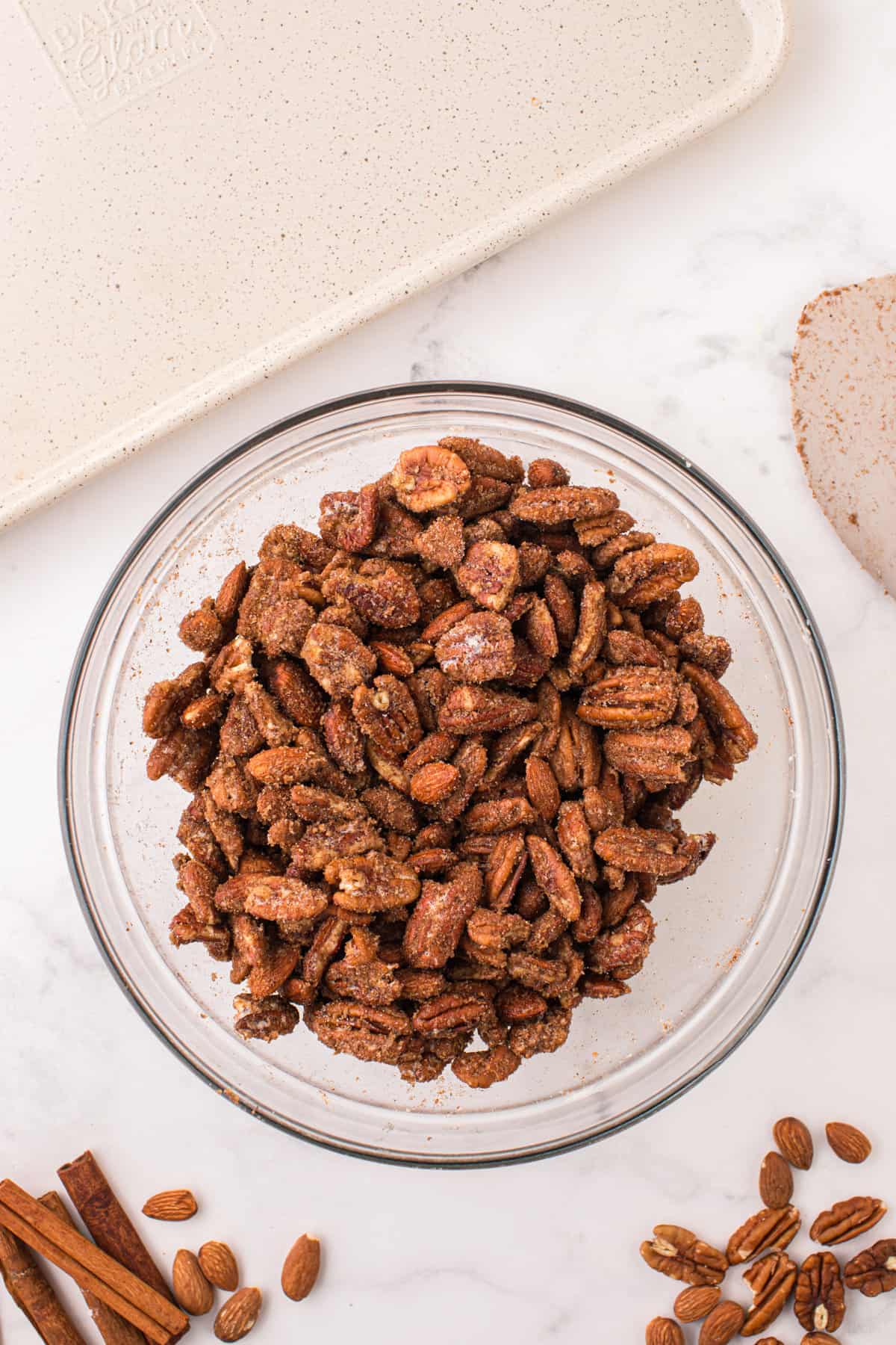 Almonds and pecan coated in sugar mixture in mixing bowl.