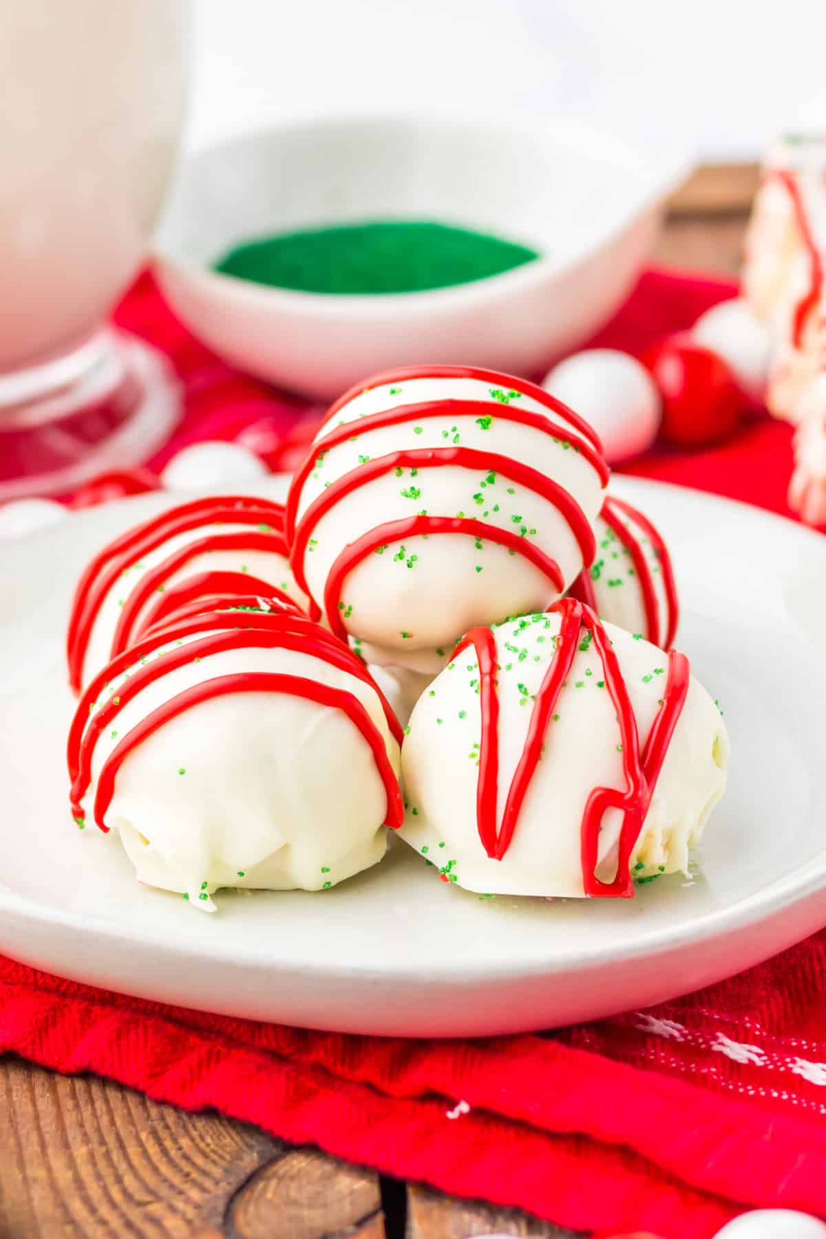 Little Debbie Christmas Tree Cake Balls on white plate with green sanding sugar and glass of milk behind them.