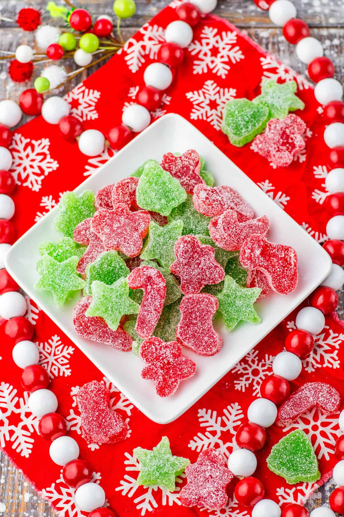 Christmas gumdrop candy on a square white plate surrounded by red and white holiday decor and additional gumdrop candies.