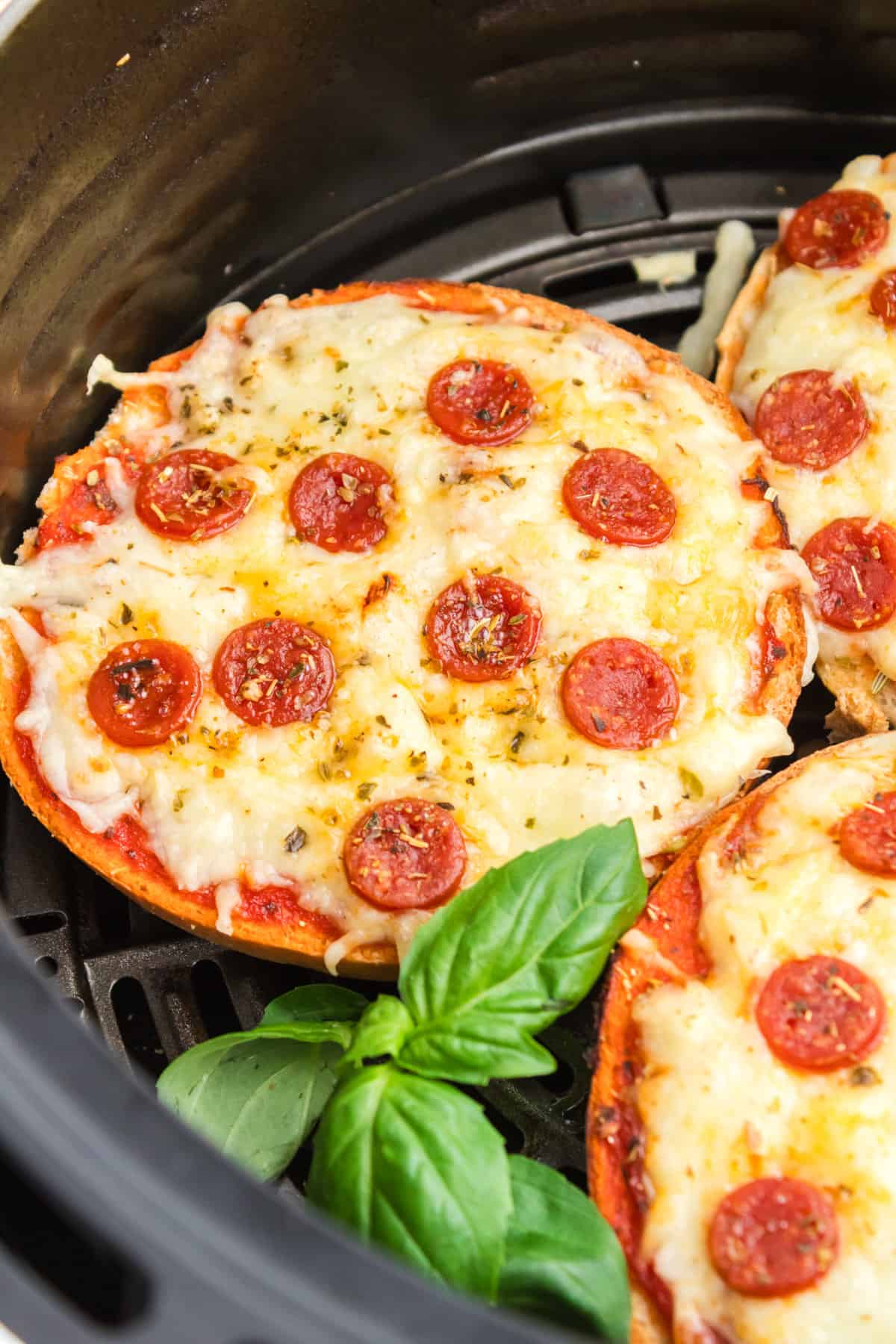 Air Fryer Pizza Bagels with pepperoni and and seasonings in the basket of an air fryer.