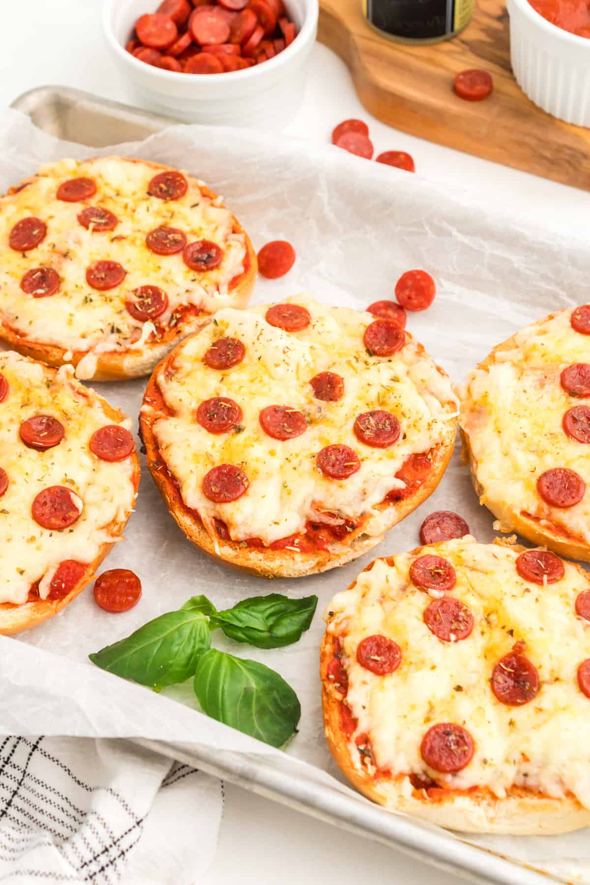 Air fryer bagel pizzas on white serving platter with fresh basil.