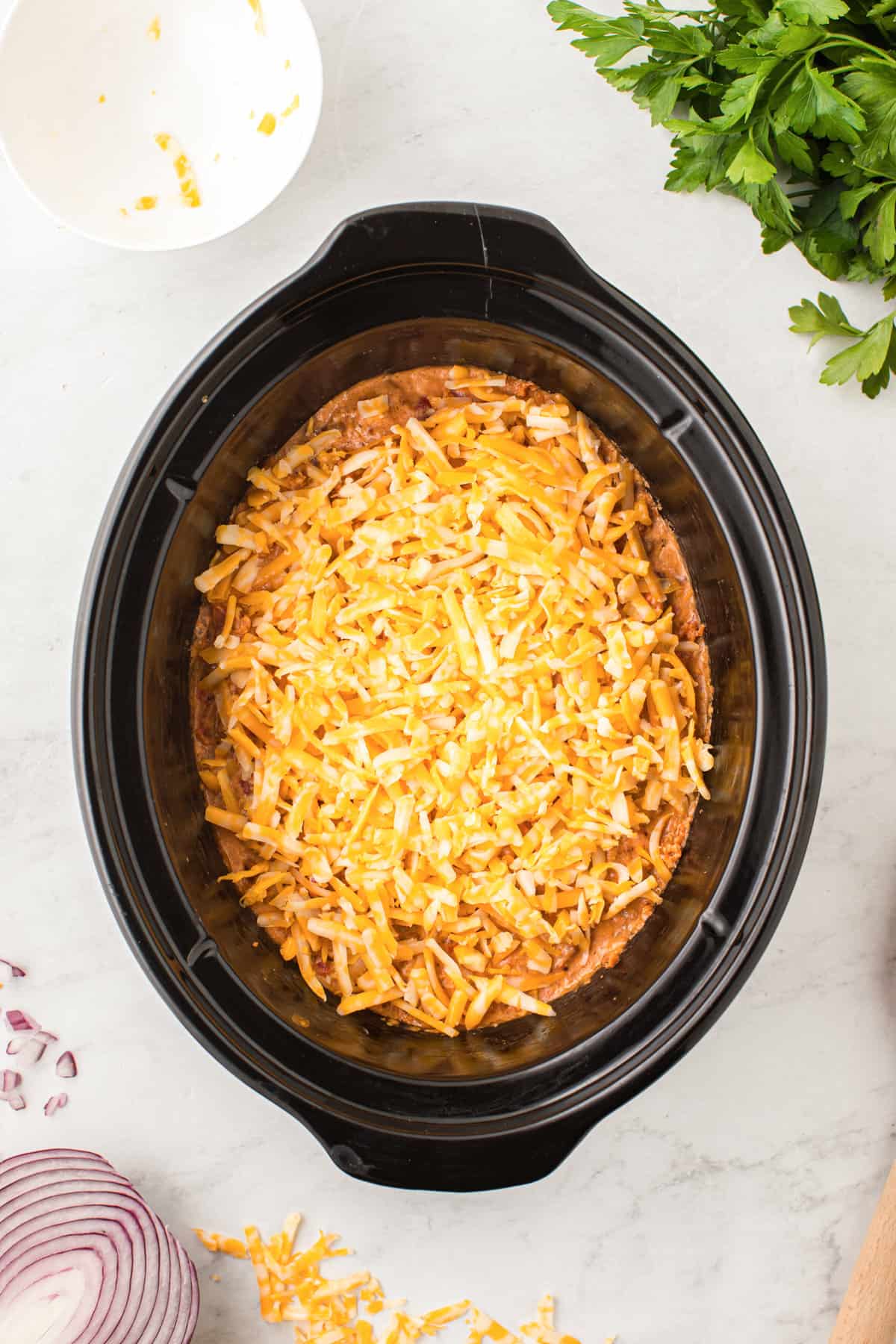 Shredded colby jack cheese sprinkled on top of dip in the slow cooker.