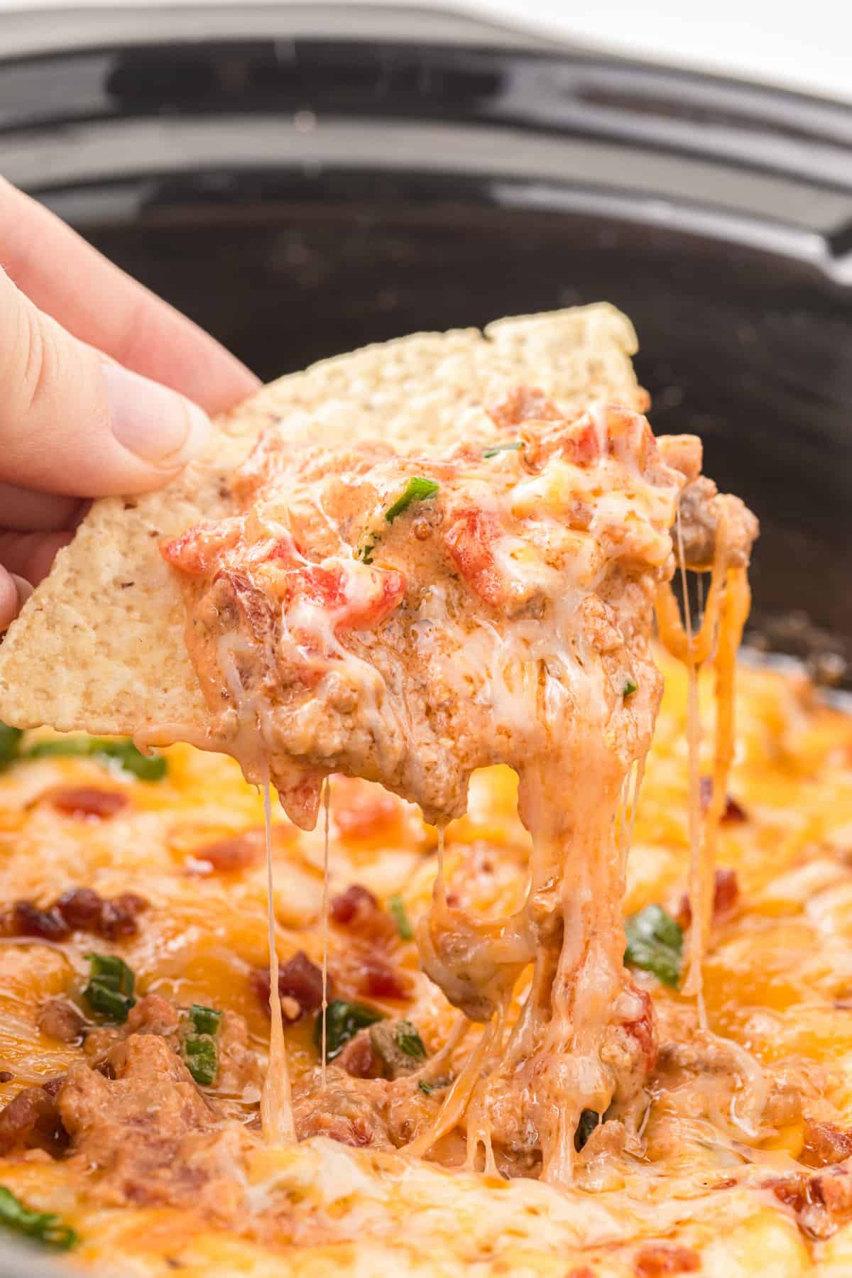 Tortilla chip scooping cheeseburger crock pot dip with lots of melted cheese.