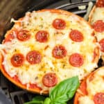 Air fryer pizza bagels with mini pepperonis in an air fryer basket.