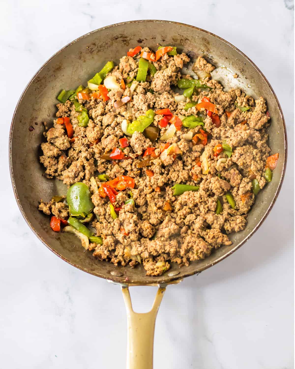 Browned ground beef, peppers, and onions in a frying pan.