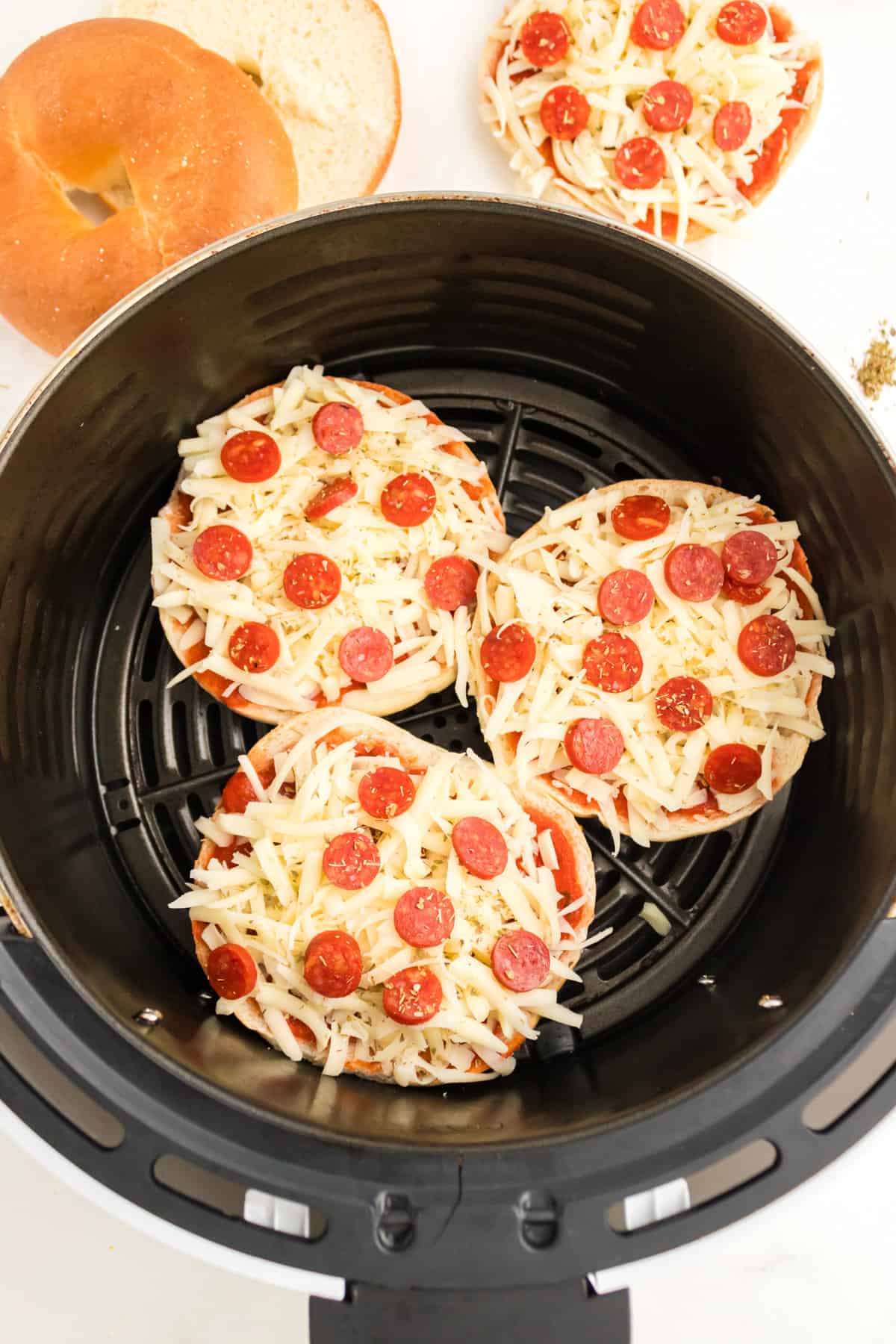 Three uncooked pizza bagels in the basket of an air fryer.
