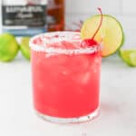 Pink Margarita drink in a rocks glass with salted rim and lime wheel and maraschino cherry garnish.
