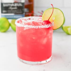 Pink Margarita drink in a rocks glass with salted rim and lime wheel and maraschino cherry garnish.