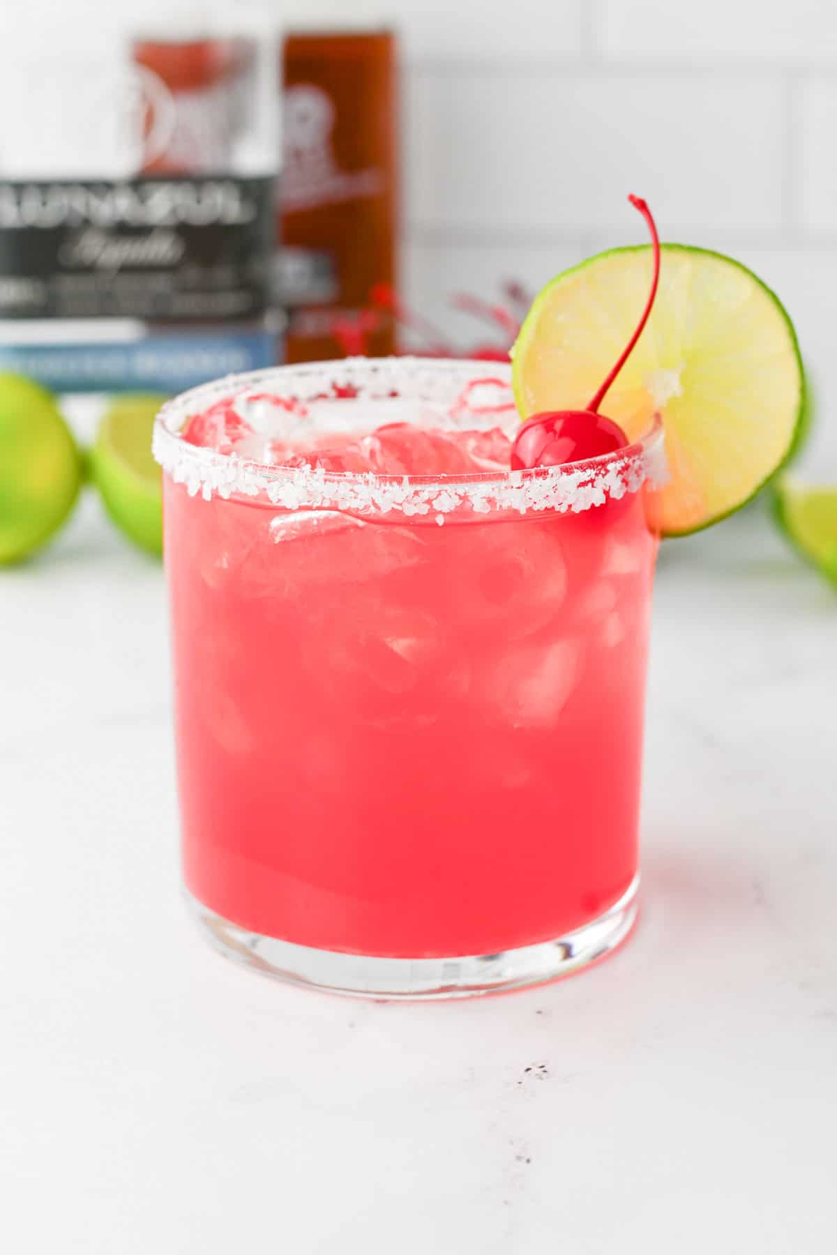 Pink Margarita with salted rim and lime wheel and cherry for garnish. 