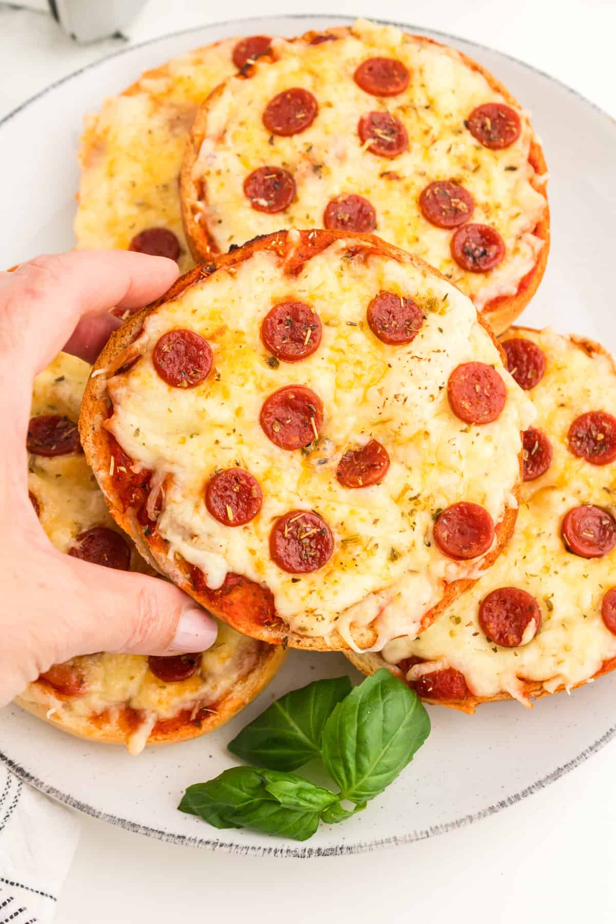 Hand holding a homemade pepperoni pizza bagel.
