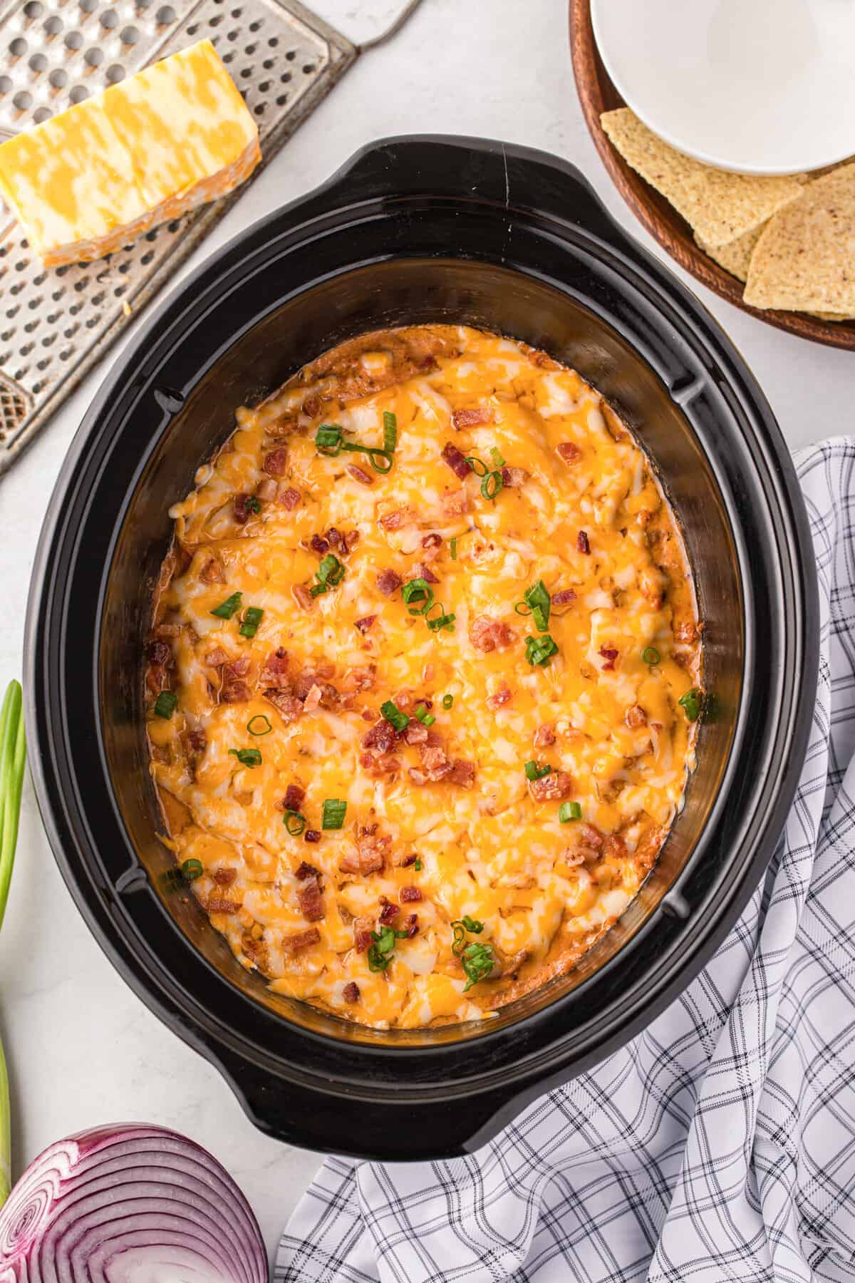 Crockpot cheeseburger dip topped with chopped green onions and bacon and served with tortilla chips.