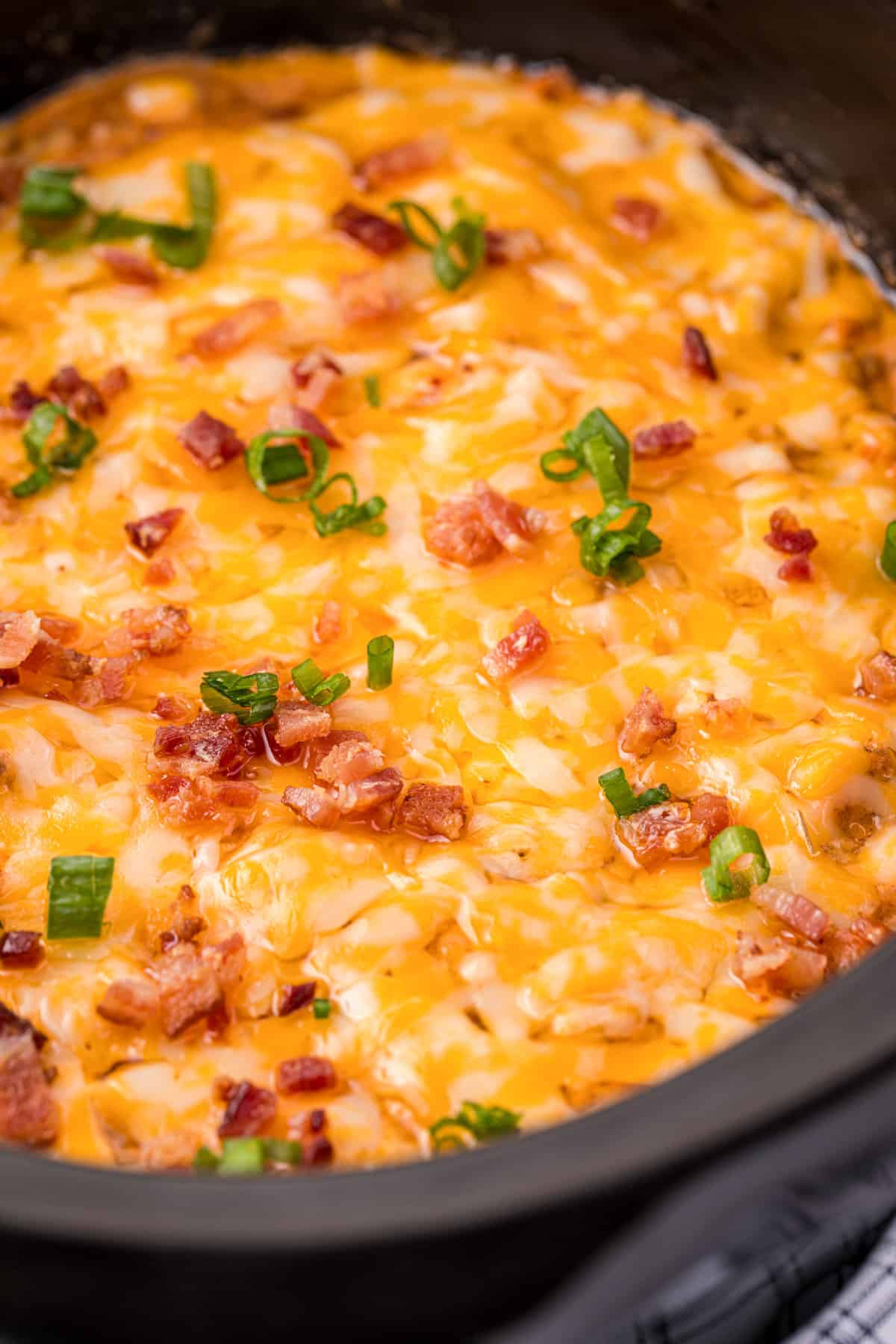 Slow cooker cheeseburger dip topped with melted cheese, chopped bacon, and green onions.