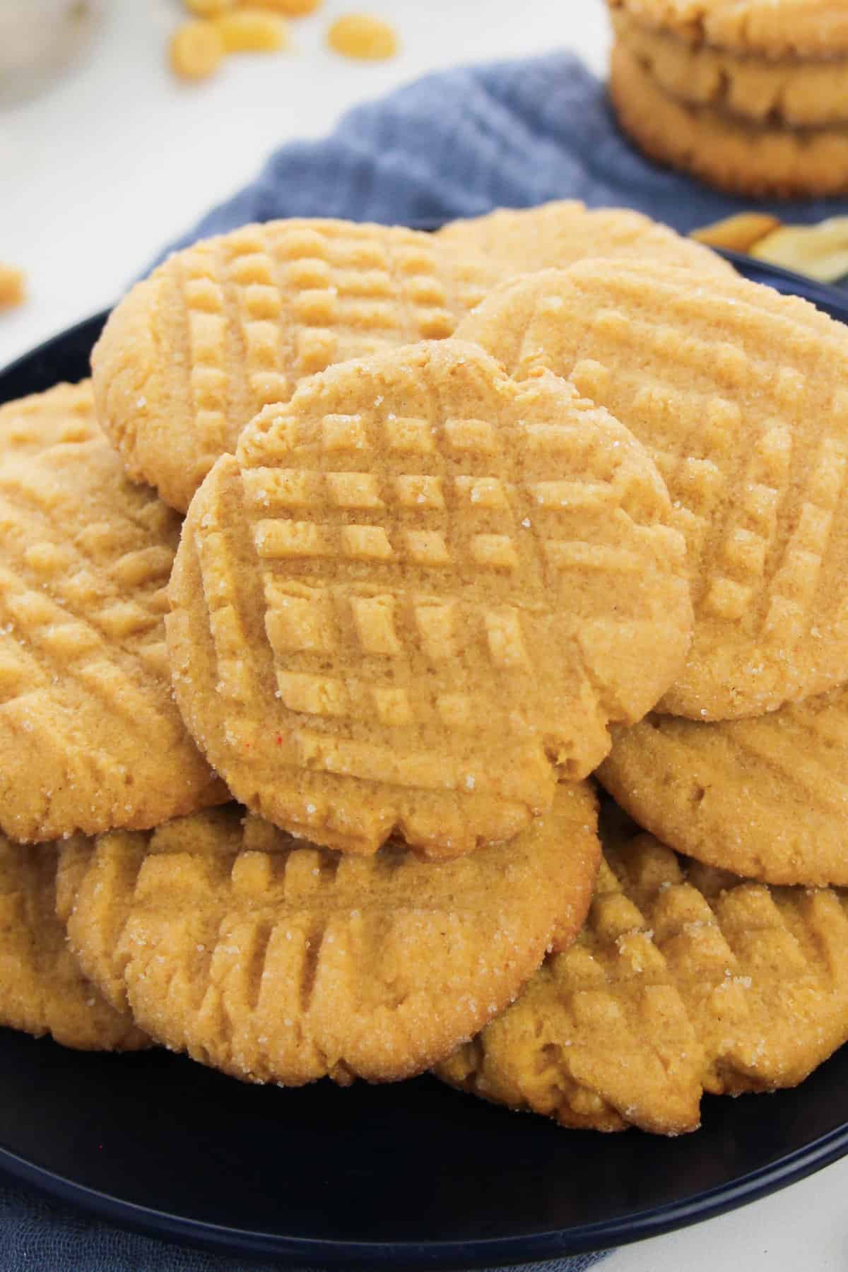 Batch of cake mix peanut butter cookies with criss-cross pattern pressed in the top piled on a black plate.