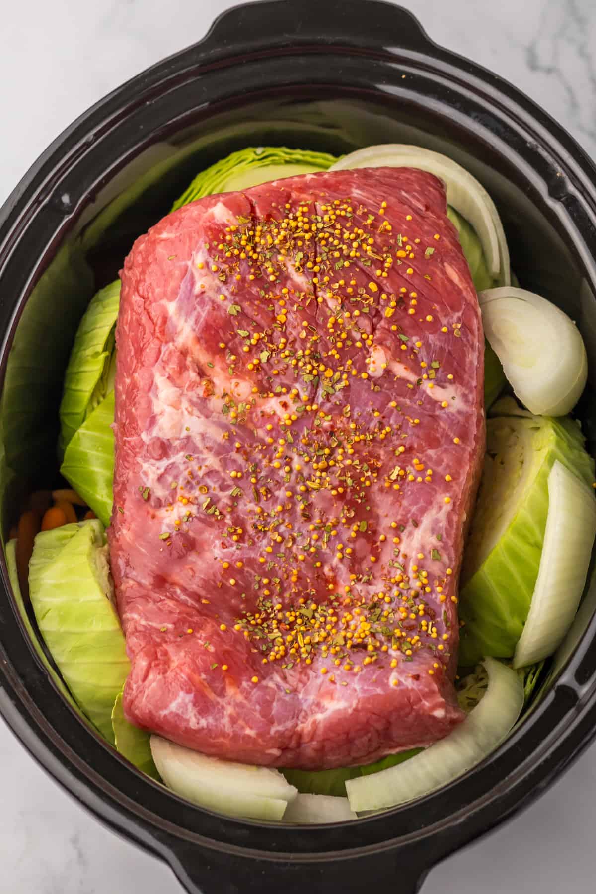 Corned beef in crockpot surrounded by cabbage, onions, and carrots.