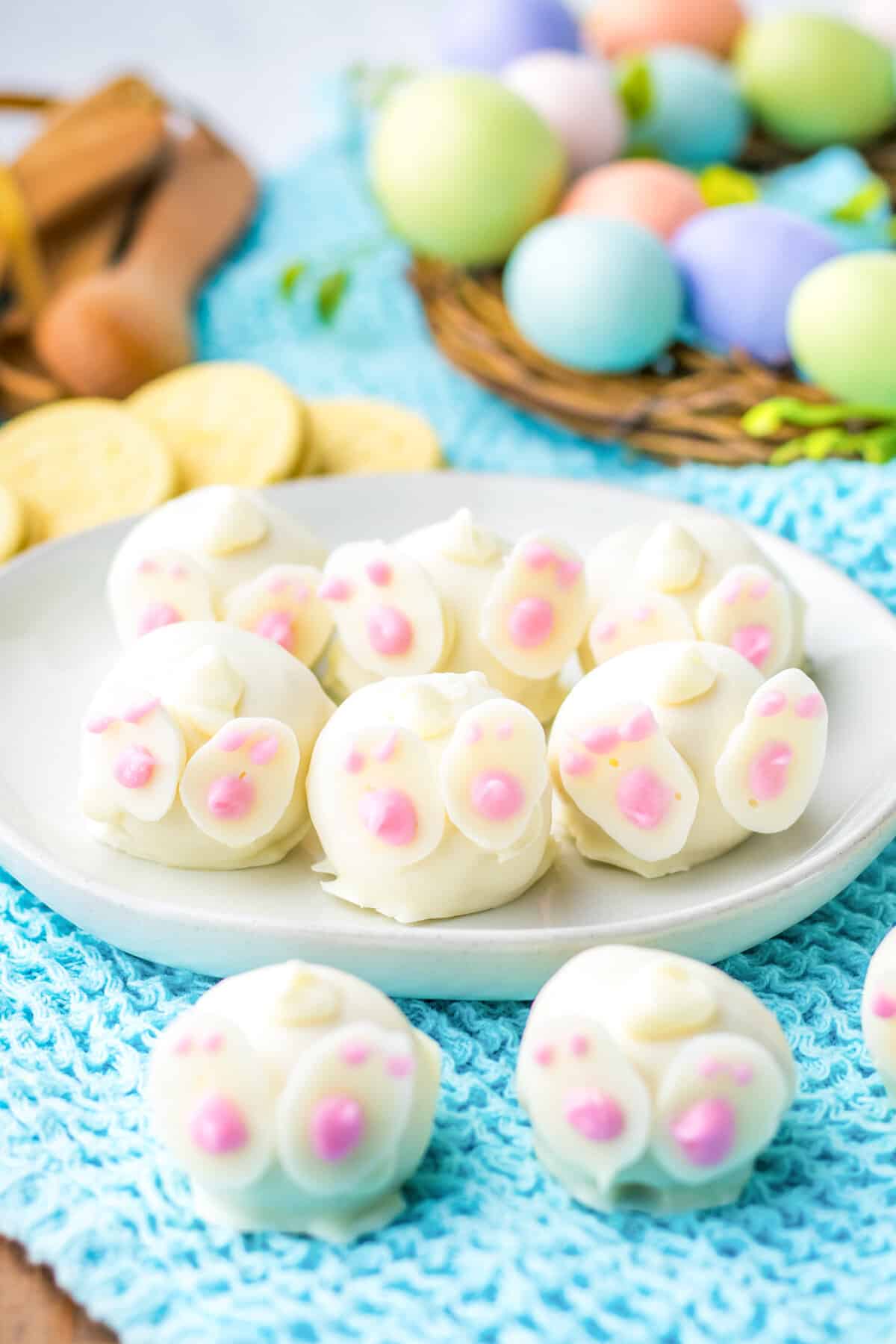 Bunny oreo balls decorated with feet and tails to look like bunny butts. Lemon oreo cookies and easter eggs are in the background.