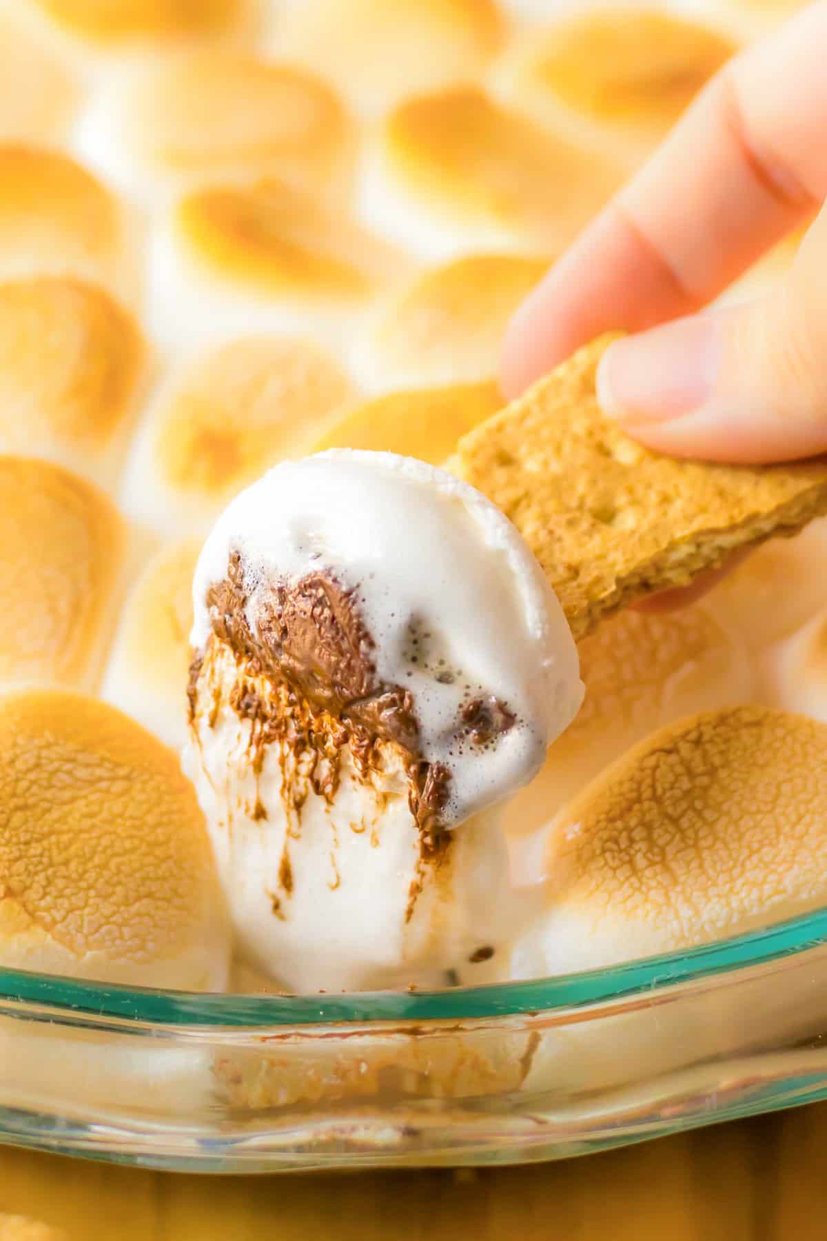 Graham cracker being dipped in s'mores dip made with marshmallows and chocolate chips.