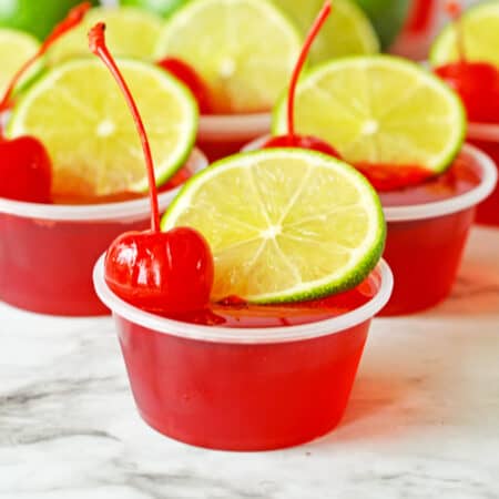 Cherry limeade jello shots made with vodka and topped with lime and cherry.