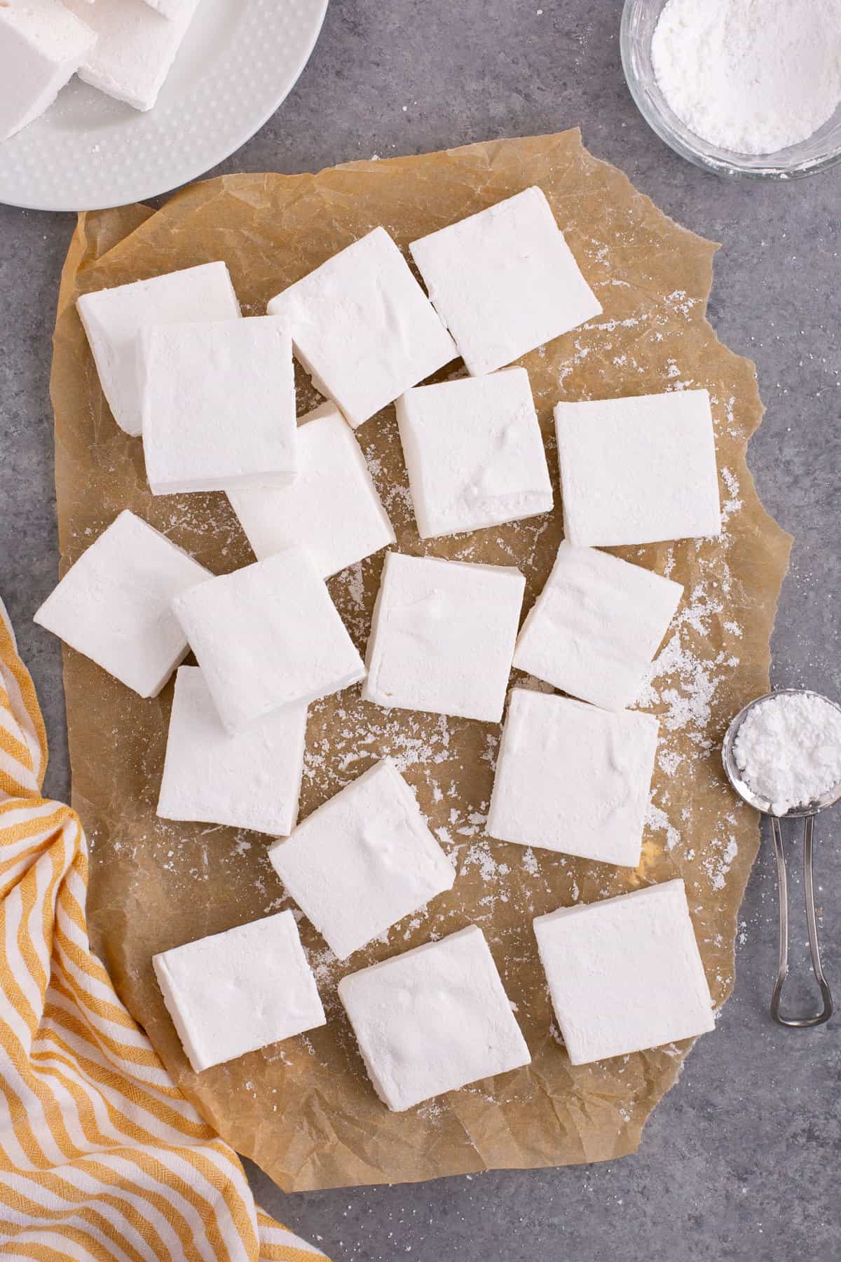Homemade marshmallows on brown parchment paper with dusting of confectioners sugar.