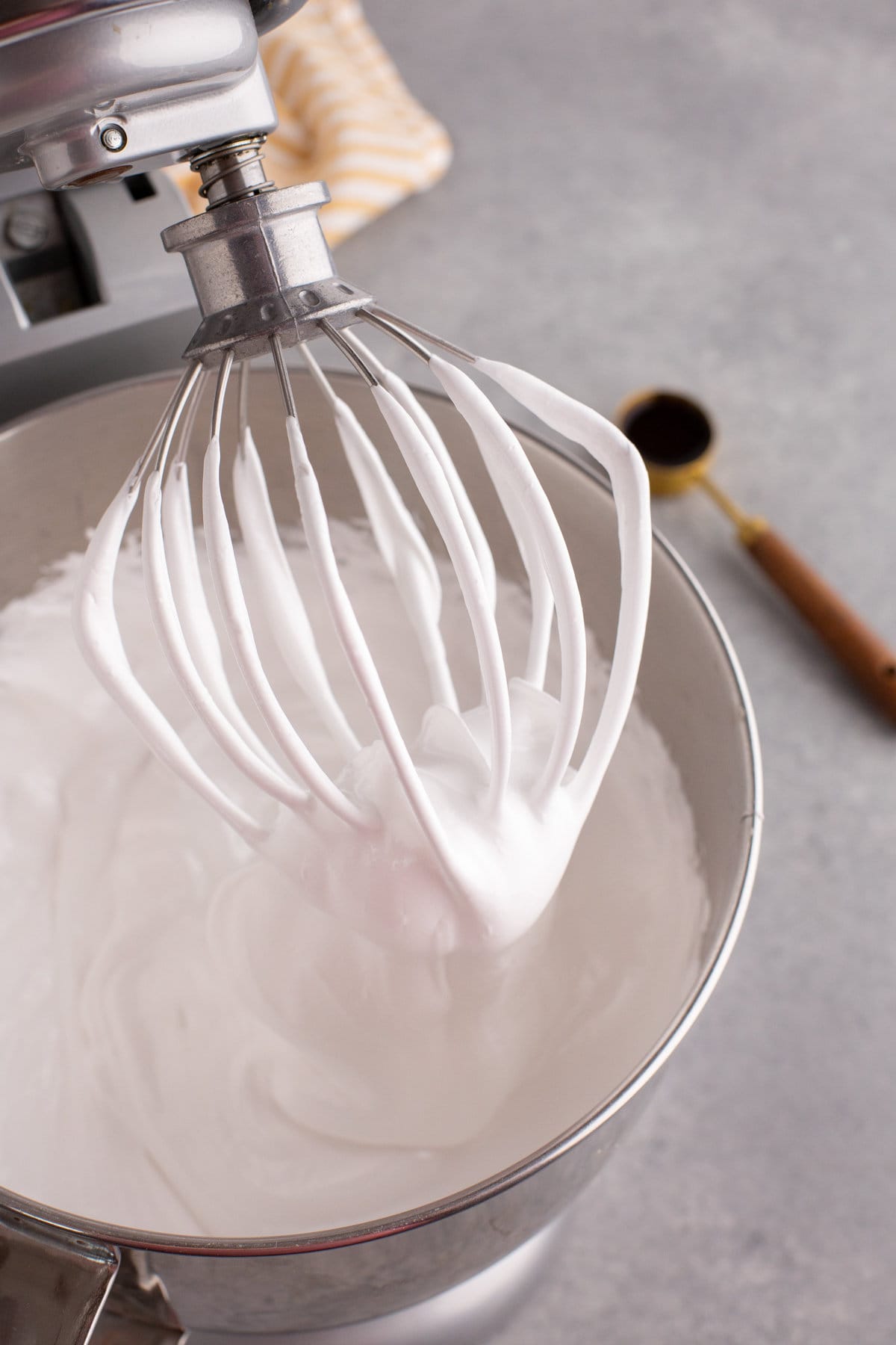 Stand mixer head tilted back to show whisk attachment with white fluffy marshmallow mixture on it.