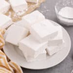 Fluffy homemade marshmallows piled on white plate coated in powdered sugar.