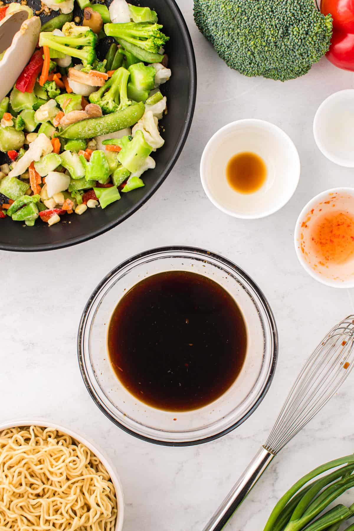 Dark brown stir-fry sauce in small glass bowl surrounded by other ingredients for the dish.