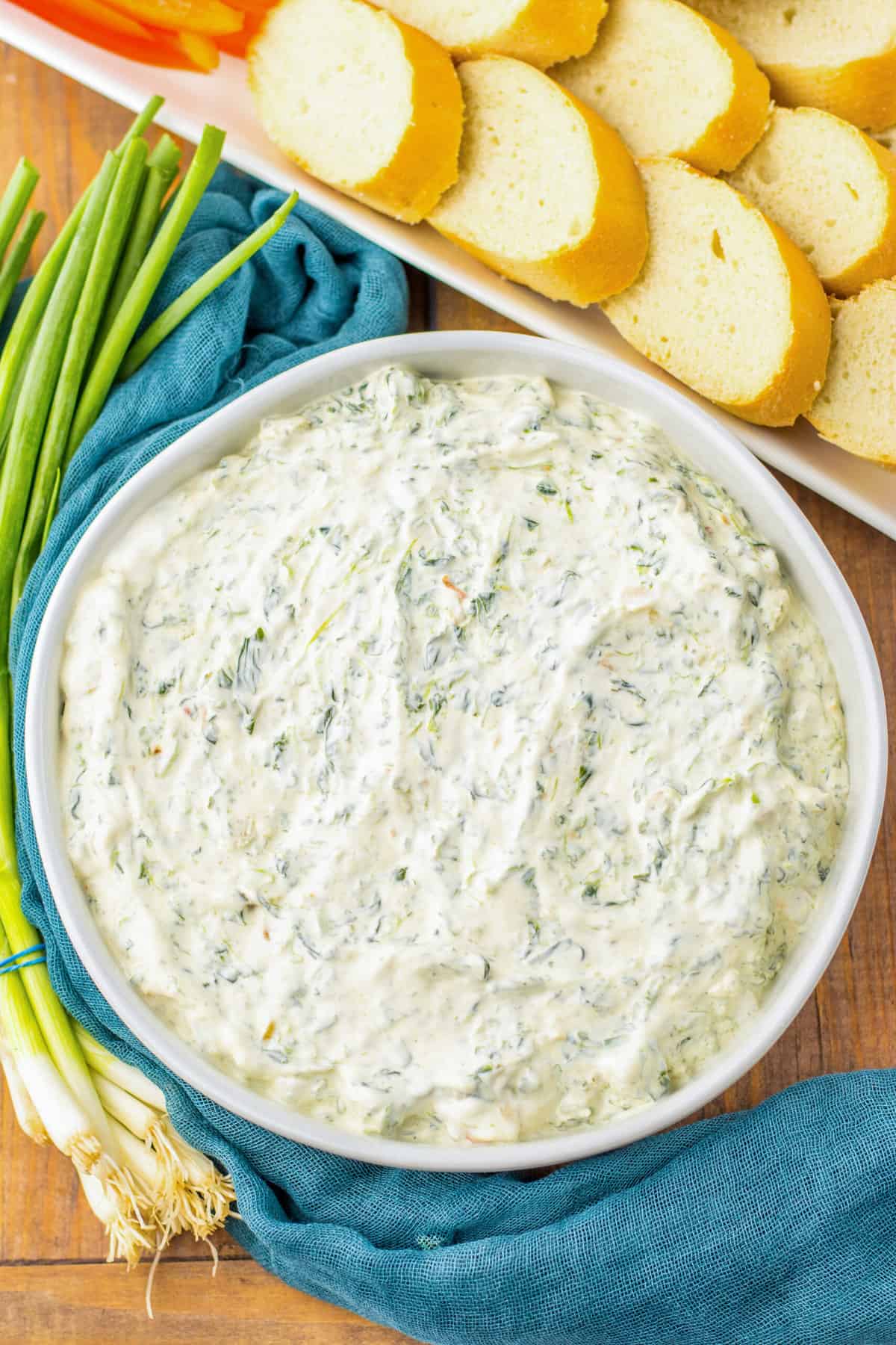 Classic Knorr spinach dip in a white serving bowl next to a tray of bread and veggies for dipping.