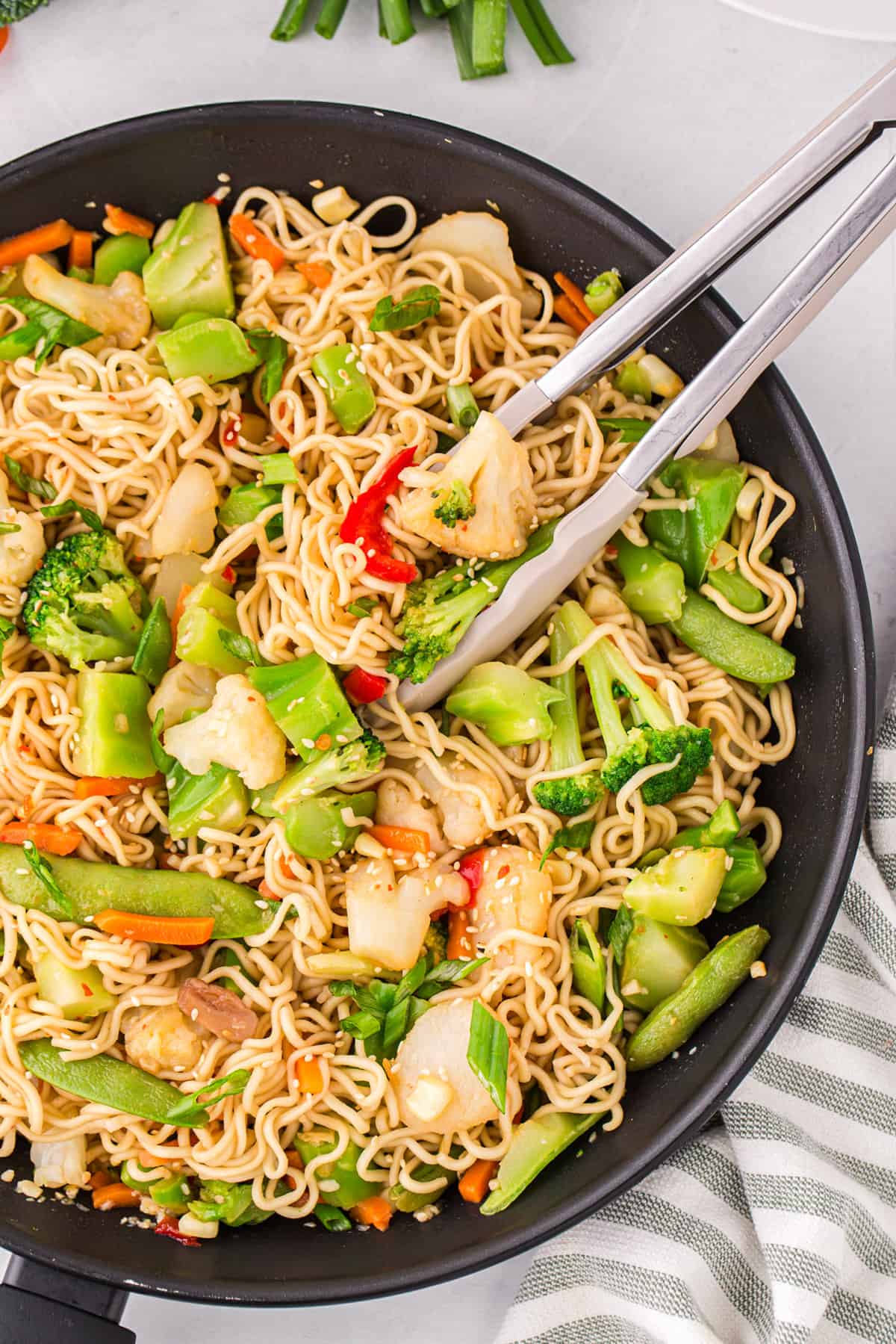 Ramen noodle stir fry in pan with tongs for serving.