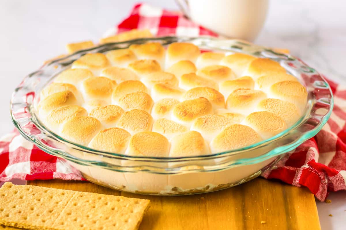 Smores dip topped with golden brown toasted marshmallows in a glass pie dish with graham crackers for serving.