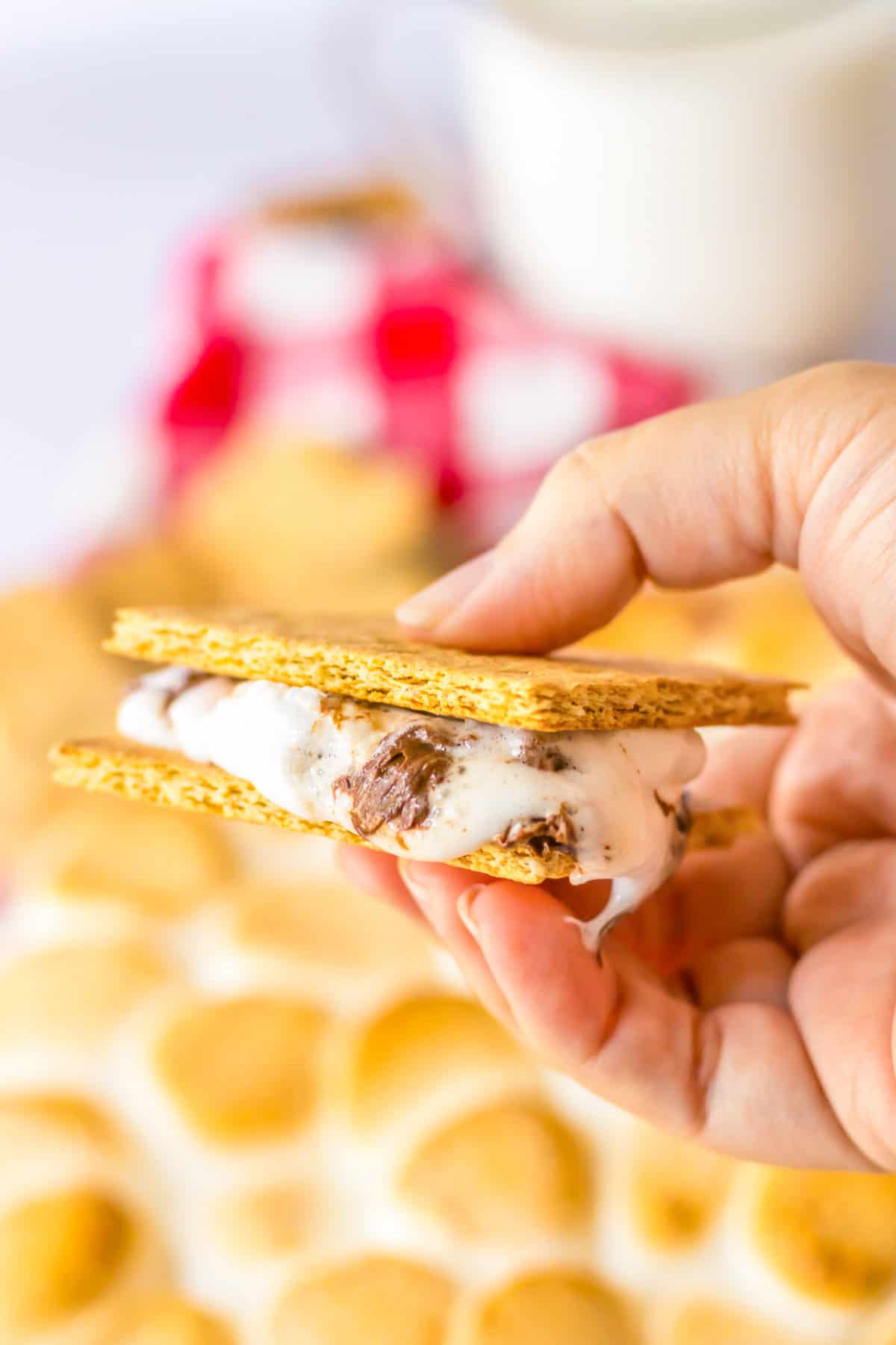 Hand holding s'mores dip sandwiches between two graham cracker squares.