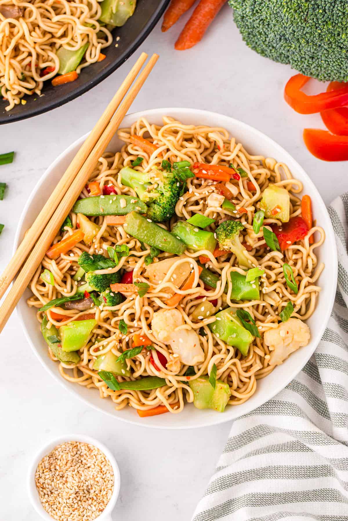 Ramen stir fry with broccoli, snap peas, carrots, bell peppers, cauliflower, mushrooms, sesame seeds, and green onions served in a large bowl with chop sticks.