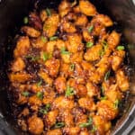 Slow Cooker orange chicken in bowl of a crockpot topped with sesame seeds and scallions.