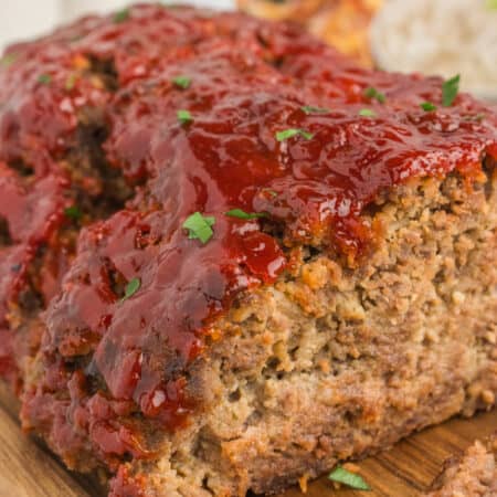 Lipton onion soup mix meatloaf with ketchup glaze on a cutting board with box of soup mix in background.