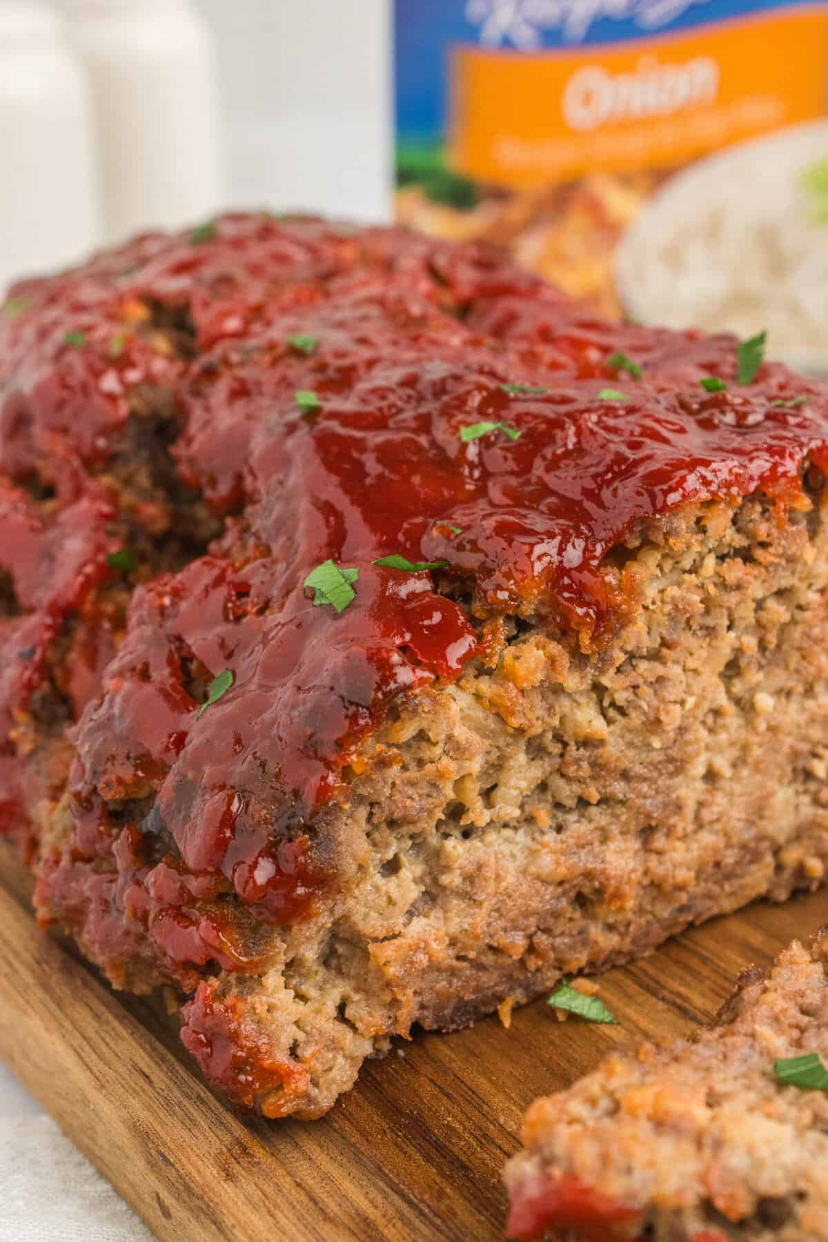 Lipton onion soup mix meatloaf with ketchup glaze on a cutting board with box of soup mix in background.