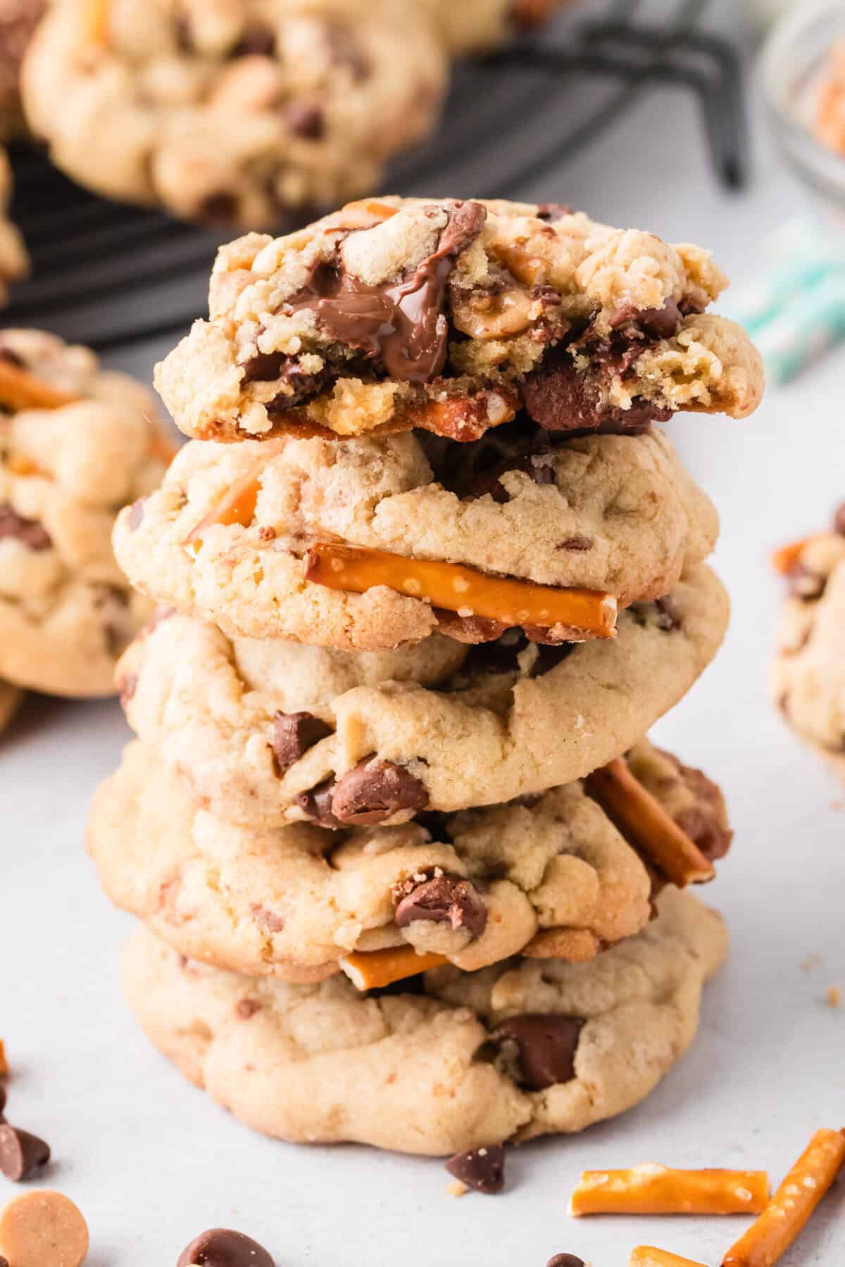 Everything but the kitchen sink cookies stacked on top of one another with a bite taken out of the top cookie to show melted chocolate chips.