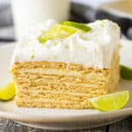 Slice of key lime icebox cake with layers of key lime custard and graham crackers on white plate garnished with slice of key lime.