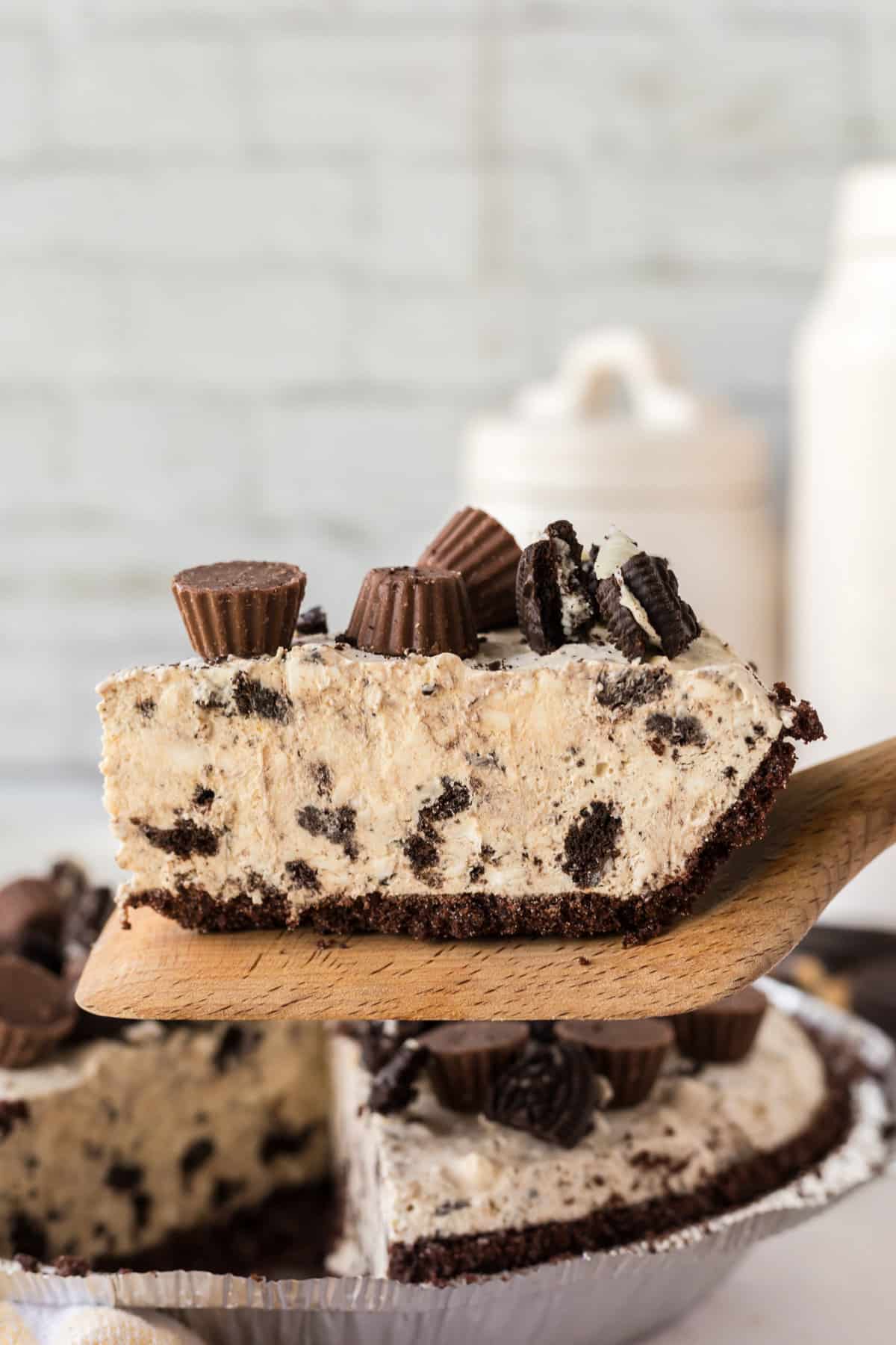 Slice of no bake peanut butter pie with oreo crust being lifted from pie with wooden server.