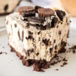 Slice of Oreo Peanut Butter Pie with chocolate cookie crust, peanut butter filling with crushed oreos, and reese's and oreos on top. A forkfull has been taken out of the pie.