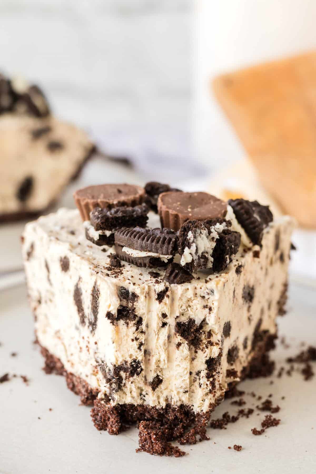 Slice of Oreo Peanut Butter Pie with chocolate crust, creamy peanut butter filling with crushed oreos, and mini reese's and chopped oreos on top. A forkfull has been taken out of the pie.