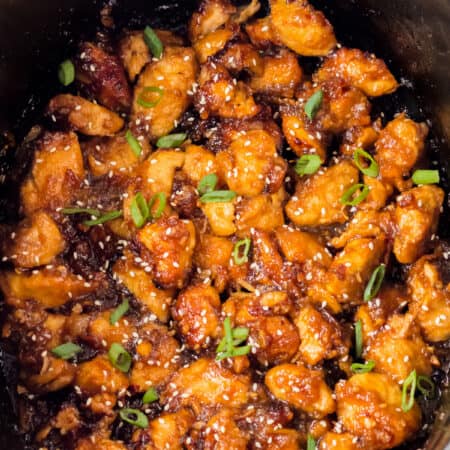 Orange chicken in the slow cooker garnished with sesame seeds and scallions.