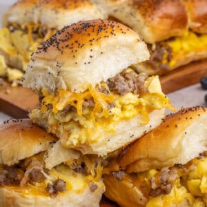 3 Sausage egg and cheese Hawaiian Roll Breakfast Sliders stacked on top of one another with more in the background.