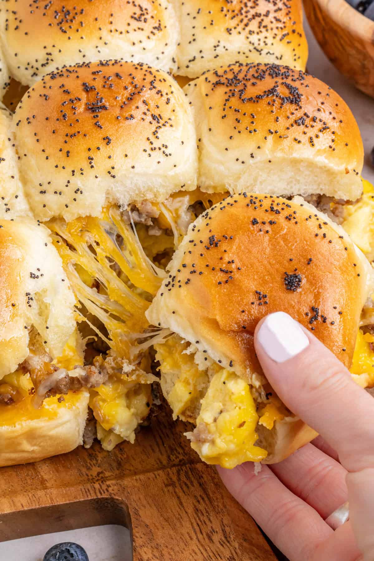 Hand pulling a single cheesy breakfast slider off the sheet of sliders.