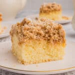 Slice of New York style crumb cake with thick layer of crumb topping. Another slice and a teapot are in the background.