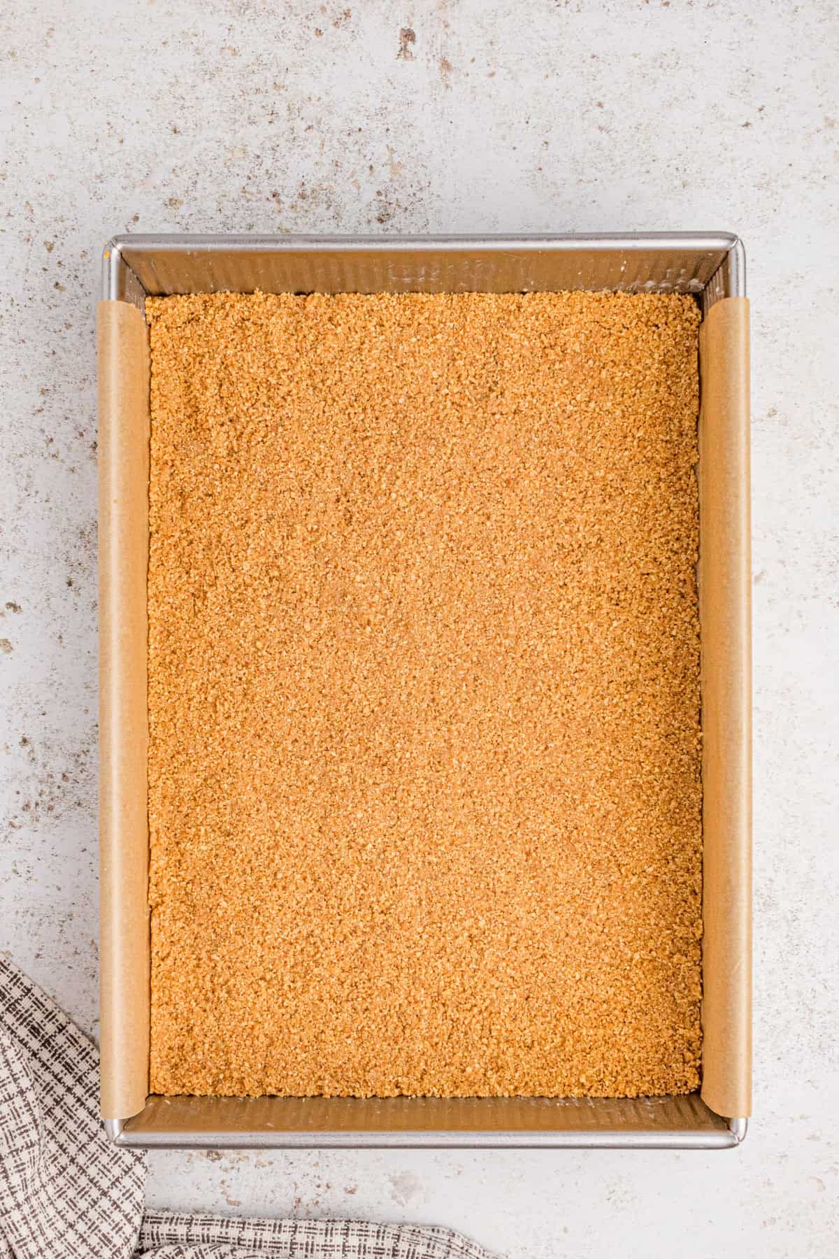 Graham cracker crust pressed evenly into the bottom of a lined baking pan.