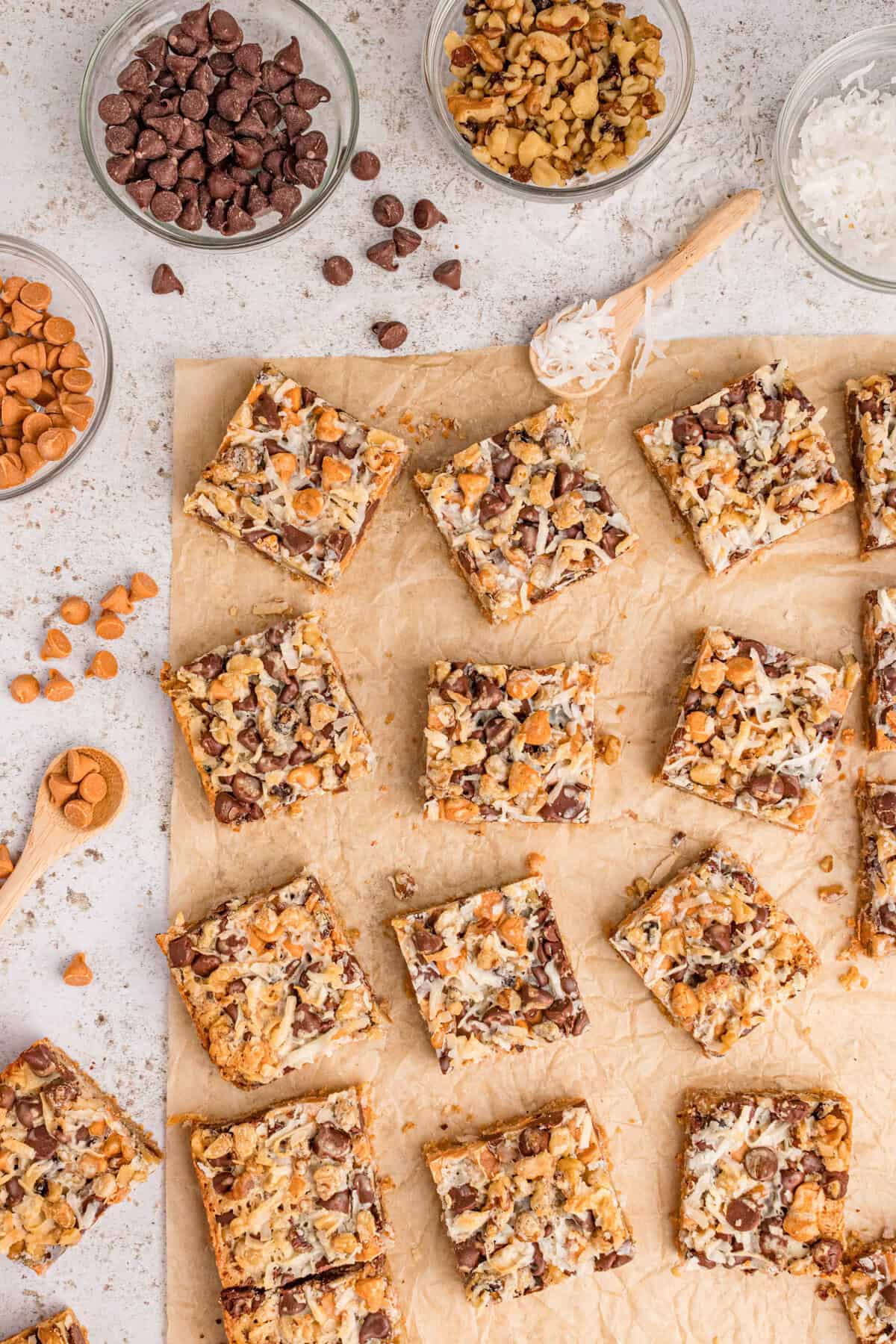 Square seven layer bars on parchment paper with chocolate chips, coconut, nuts, and buttersotch chips.